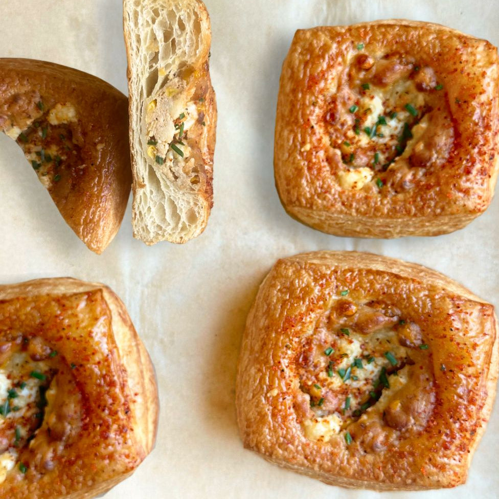 Four baked pastries with melted cheese, herbs and corn on a baking sheet lined with parchment paper.